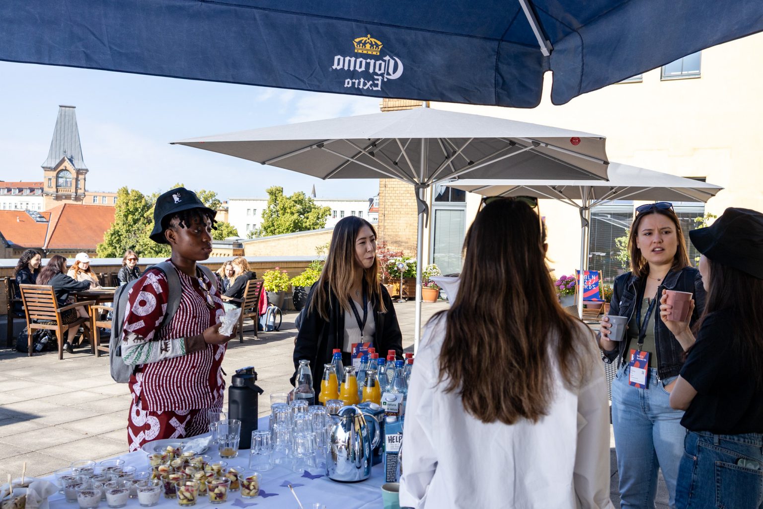 A group of women* speakers talking to each other on the roof top terrace. In the background there is another group of women sitting around a table.