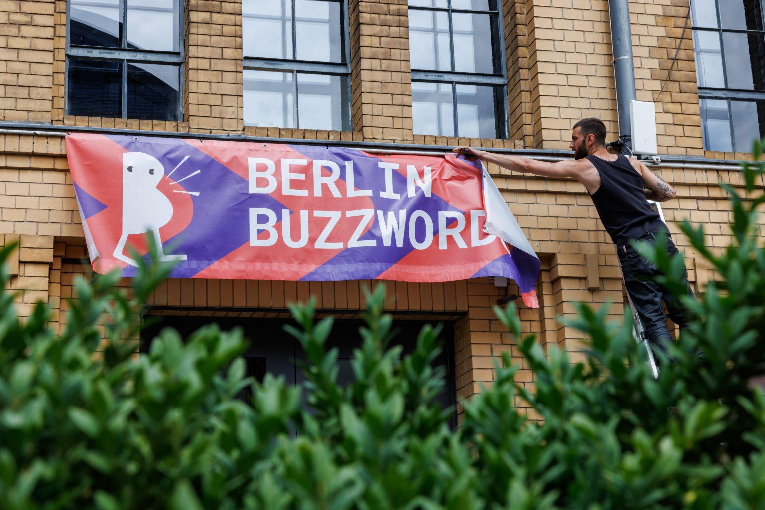 A man on a ladder fixing or removing a Berlin Buzzwords banner.
